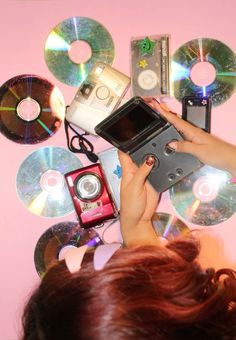 a woman holding up a camera next to several cd's on a pink wall