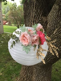 a paper lantern hanging from a tree with pink flowers on it and greenery in the center