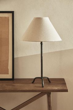 a lamp sitting on top of a wooden table next to a framed photo and a painting