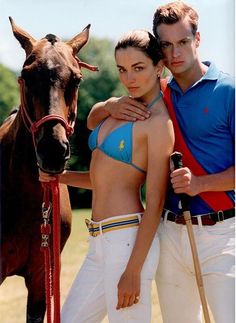 a man and woman standing next to a horse wearing bathing suits with their arms around each other