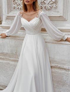 a woman in a white wedding dress leaning against a wall with her hands on her hips