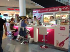 a woman is getting her nails done at the nail bar in an airport terminal with people standing around