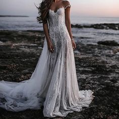 a woman standing on top of a rocky beach next to the ocean wearing a wedding dress