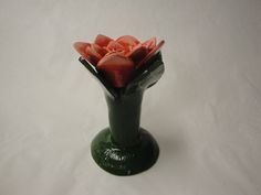 a green vase filled with red flowers on top of a white table