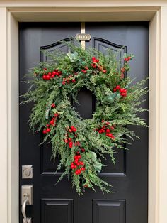 a christmas wreath hanging on the front door with holly and red berries, greenery