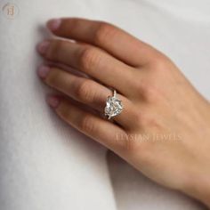 a woman's hand with a diamond ring on her left hand, wearing a white shirt