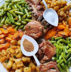 a white plate topped with meat and veggies next to seasoning spoons