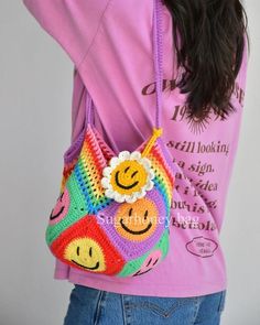 a woman wearing a pink shirt is holding a crocheted bag with smiley faces on it