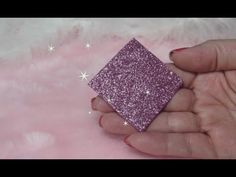 a hand holding a purple glittered square object in it's left hand on a pink fur surface