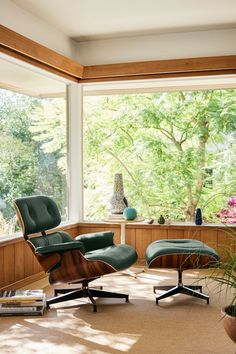 an eames chair and ottoman in front of a window with trees outside the window