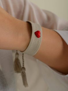 a woman's arm with a red heart and tasseled bracelet on it