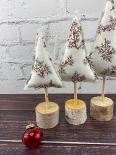 three small christmas trees sitting on top of wooden logs next to a red ornament