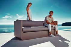 a man and woman sitting on top of a couch next to each other near the ocean