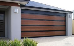 a house with a large wooden garage door in front of it and two plants on the sidewalk