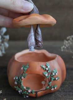 a hand is holding an orange vase with two bats on it and flowers in the background