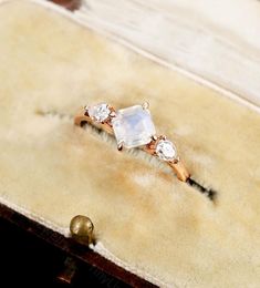 an engagement ring with three diamonds on it sitting on top of a velvet box next to two bells