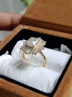 an engagement ring in a wooden box on top of a white cloth covered napkins