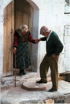 an old man and woman standing in front of a door