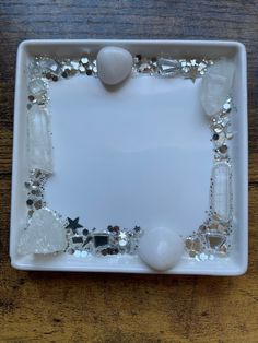 a white square plate with some beads and stones in it on a wooden table top