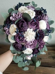 a bridal bouquet with purple and white flowers is held by someone's hand