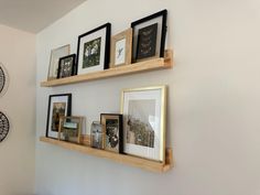 three wooden shelves with pictures on them against the wall and two clocks hanging above it