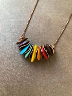 a multicolored necklace is hanging from a ball chain on a gray table top