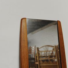 a wooden frame holding a mirror with chairs in the reflection and a white wall behind it