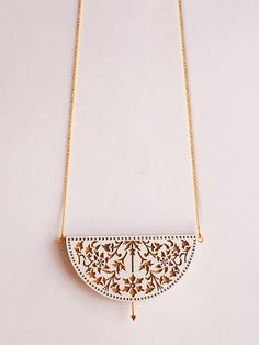 a white and gold necklace with an intricate design on the front, hanging from a golden chain