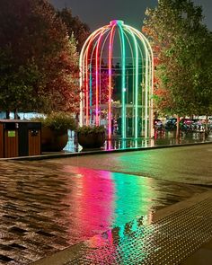 a colorful light display in the middle of a city street at night with reflections on the wet pavement