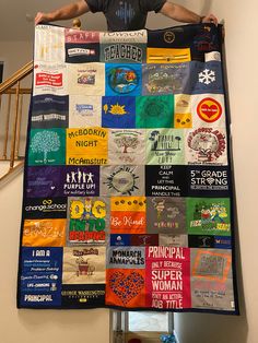 a man standing on top of a ladder holding up a large quilt made out of t - shirts