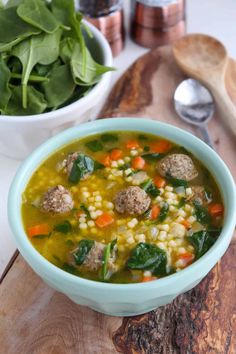 a bowl of soup with meatballs, corn and spinach next to a wooden spoon