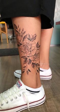 a woman's leg with flowers on it and white shoes in the foreground