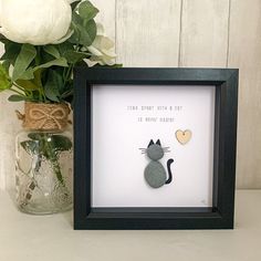 there is a framed picture with a cat and heart on it next to a vase filled with flowers