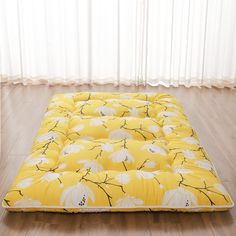 a yellow and white flower print futon mattress on the floor in front of a window