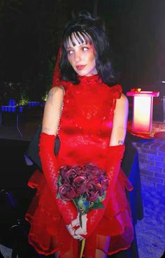 a woman in a red dress holding a bouquet of flowers and wearing gloves with her hands on her hips