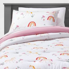 a bed with pink and white sheets and rainbows on the comforter, along with matching pillow cases