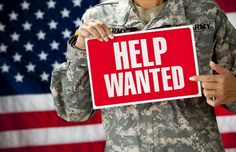 a man holding up a red help wanted sign in front of an american flag with the caption help wanted