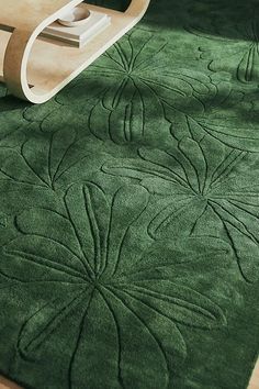 a green rug with an intricate design on the floor next to a wooden table and chair