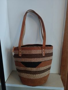 Geometrical earth tone sisal tote bag. Unique and stylish colorful sisal kiondo bag with stitched leather straps, pocket lining and zipper. Patterns and sizes slightly vary because weaving and stiching is done by hand. Ideal as a beach bag, shopping basket, market basket or storage basket. This unique tote bag is handmade by a group of ladies in a remote rural village in Machakos, Kenya. Do not clean with brush or water. If the bag gets wet, please dry to avoid dampness.  Leather type used is bo Modern Bags With Leather Handles For Market, Brown Bucket Shoulder Bag With Handles, Modern Rectangular Bags For Market, Brown Woven Shoulder Bag For Everyday, Casual Brown Basket Bag, Brown Satchel Beach Bag For Daily Use, Handheld Brown Straw Bag For Travel, Large Capacity Brown Crochet Satchel Bag, Brown Woven Shoulder Beach Bag