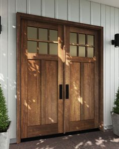 two wooden doors on the side of a white building with potted plants in front