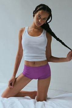 a woman in purple shorts and white tank top sitting on a bed posing for the camera