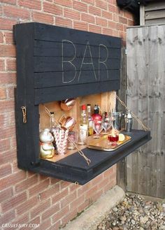 an outdoor bar with drinks and snacks on the outside, in front of a brick wall