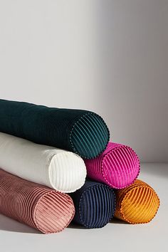 four different colored pillows stacked on top of each other in front of a white wall