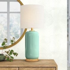 a table lamp sitting on top of a wooden dresser next to a mirror and potted plant