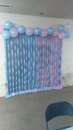 blue and pink balloons are hanging on the wall in front of a party curtain with streamers