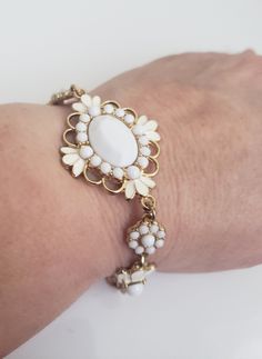 "Adjustable gold tone bracelet featuring medallions of milk glass and white enamel petals or feathers on a simple gold chain link band. Hang tag with stylized \"C\".  Measure 1 1/4\" at the widest and total length is 8 1/2\".  In very good condition with no broken or missing milk stones, intact enamel, and shiny gold tone metal. See the photos.  Do browse our other items. We combine shipping for savings." White Metal Bracelet Jewelry, White Metal Chain Bracelet, White Metal Jewelry With Extender, Adjustable White Metal Charm Bracelet, White Adjustable Chain Bracelet, Adjustable White Chain Bracelet With Extender, Vintage Cream Bracelet, Vintage White Metal Jewelry, White Costume Jewelry In Metal