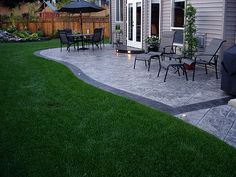 a patio with chairs and an umbrella in the back yard, next to a house