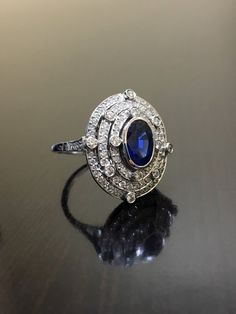 DeKara Designs CollectionArt Deco Inspired Extremely Elegant Halo Sapphire Diamond Engagement Ring.Metal- 90% Platinum, 10% Iridium.Stones- 1 Oval Ceylon Blue Sapphire 1.25 Carats, 100 Round Diamonds F-G Color VS2 Clarity .80 Carats.  Size- 6 1/4.An Amazing Art Deco Inspired Ceylon Blue Sapphire Triple Halo Diamond Engagement.  The ring features a beautiful Ceylon Blue Sapphire that is expertly bezel set in the center.  The sapphire is surrounded by 92 pave and burnish set round sparkling diamon Luxury Sapphire Diamond Ring With Diamond Cut, Luxury Sapphire-colored Diamond Ring With Diamond Cut, Luxury Sapphire-colored Diamond Ring, Art Deco Diamond Ring With Gemstone, Luxury Oval Diamond Cut Sapphire Ring, Art Deco Halo Ring With Round Cut, Art Deco Diamond White Halo Ring With Center Stone, Art Deco White Gold Halo Ring, White Gold Art Deco Halo Ring