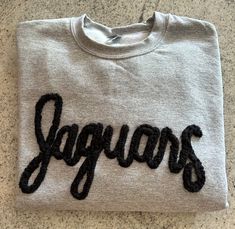 Show your school spirit in this cute sweatshirt. Comfort, casual and loose fitting, made on 50/50 cotton/poly blend shirts.  Embroidered chenille yarn, Jaguar sweatshirt.  Please message us if you have a custom color request and we will create a separate listing for custom requests.  You can follow us at the below link for chances to win giveaways and to see all of our latest creations.  https://www.facebook.com/groups/710060383256657/?ref=share&mibextid=S66gvF Winter School Spirit Sweater With Letter Print, Embroidered Logo Tops For Game Day In Fall, College Team Spirit Sweatshirt With Lettering, School Spirit Crew Sweatshirt With Ribbed Cuffs, Varsity Cotton Sweatshirt For Fall, White School Spirit Sweatshirt For Streetwear, School Spirit Sweatshirt With Team Name For Fall, College Sweatshirt With Lettering Fan Apparel, College Style Sweatshirt With Embroidered Logo For Fall