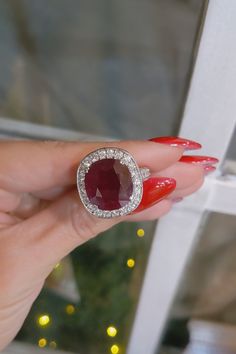 a woman's hand holding a red and white ring with diamonds on it in front of a christmas tree